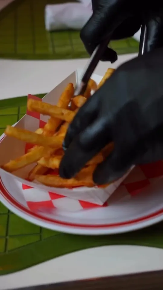 French fries being placed with tongs into a red and white paper boat on a red rimmed plate at Uncle Rocco